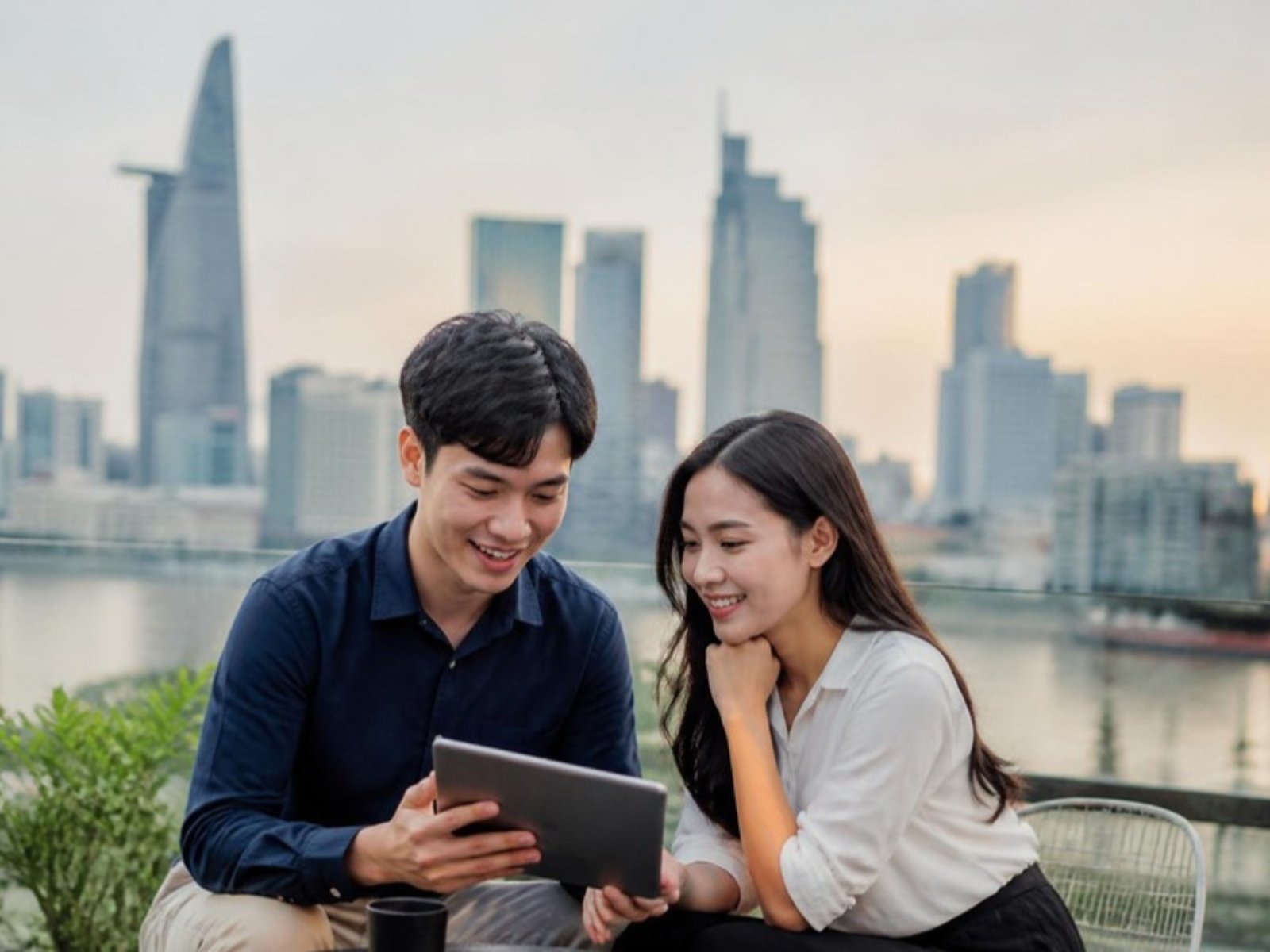 Hai người trẻ xem thông tin việc làm trên máy tính bảng, phía sau là thành phố Hồ Chí Minh